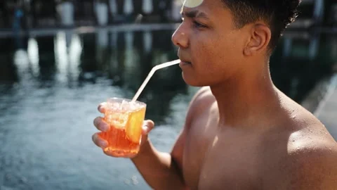 Young man holding vibrant orange cocktail with ice, lemon during summer vacation Stockbeeldmateriaal 333564953