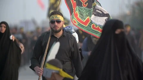A young man holds a flag while walking in Arbaeen pilgrimage Stock Footage 119242744