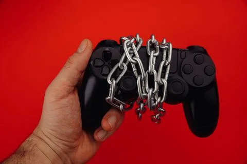 Young man holds a game controller is tied by chain isolated on red background Stock Photos