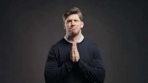 Young man holds his palms together in pleading prayer gesture, asking for help o Stock Footage 346492826