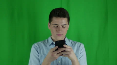 Young man holds phone texting and smiling in front of greenscreen Vidéo 59089326