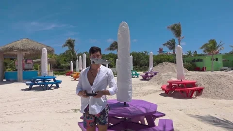 Young man holds remote controller of drone wearing beach shorts and white shirt Stock Footage 276479283