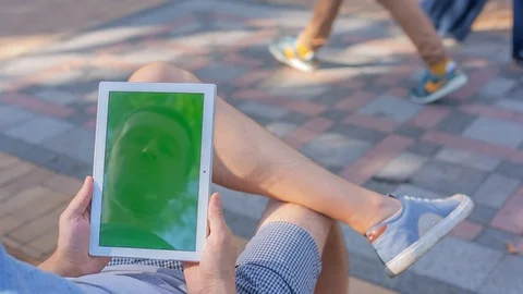 Young man holds TabletPC with green screen sitting on the bench in city park  Stock Footage 116408416