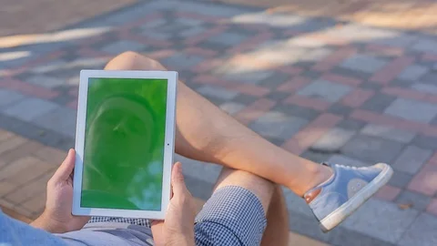 Young man holds TabletPC with green screen sitting on the bench in city park  Stock Footage 116408527