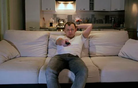 A young man at home sitting on a sofa in the evening with the remote control in  Stock Photos