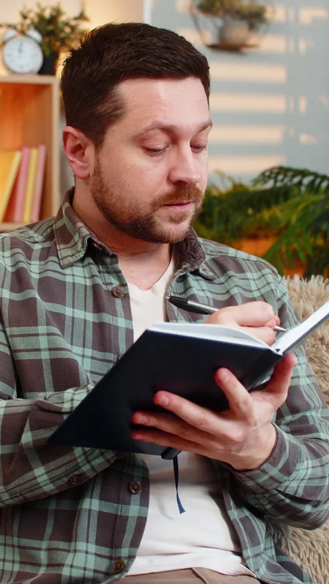 Young man on home sofa writing idea in notebook with raised finger and relieved Stock Footage 347056076