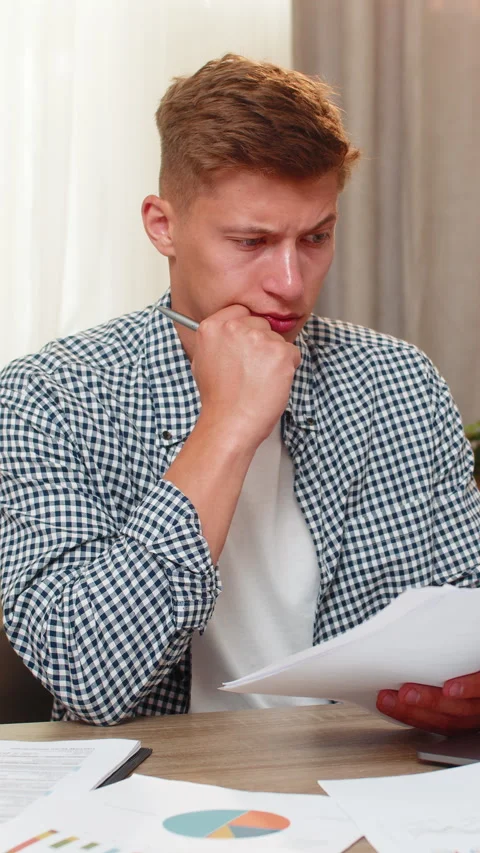 Young man on home table checking client payments while reviewing business income Stock Footage 348009232