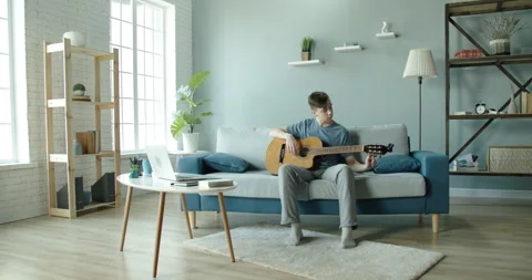 A young man is at home tuning the sound of a guitar. Video stock 130670341