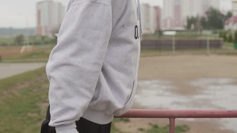 Young man in hoodie doing push-ups on parallel horizontal bars during workout Video stock 99332101
