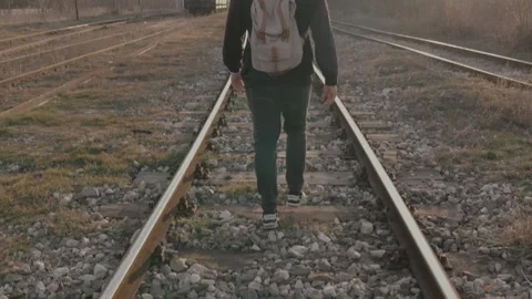 A young man with a hook and backpack walks along railroad tracks at sunset Stock Footage 302064006
