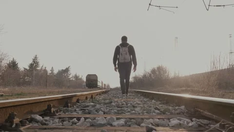 A young man with a hook and backpack walks along railroad tracks at sunset Stock Footage 302064751