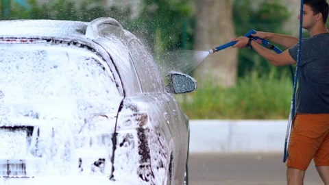 Young man hosing down his car covered in soap suds Video stock 110813603