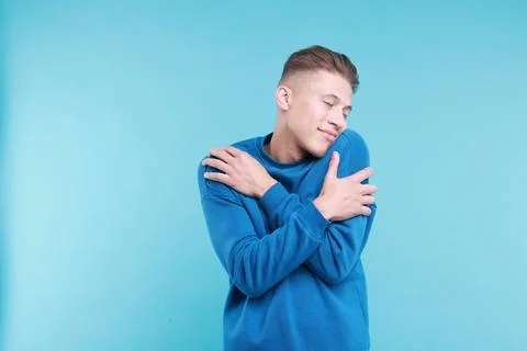 Young man hugging himself on light blue background Stock Photos
