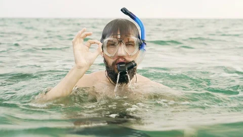 Young man immersing and emerging from water using snorkel and showing ok sign Stock Footage 119031983