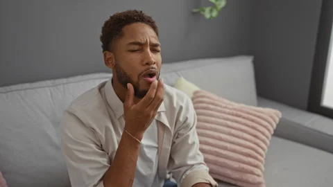 Young man indoors experiencing tooth pain while seated on a sofa in a livin.. Stock Footage 289330007