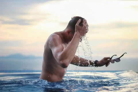 Young man in the infinity pool on a background of beautiful sunset. Stock Photos