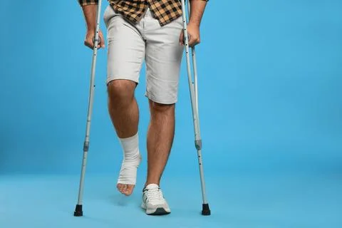 Young man with injured leg using axillary crutches on light blue background,  Stock Photos