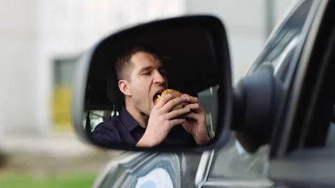 Young man inside car. Guy chewing piece of burger and enjoy the process. Tasty Stock Footage 131514852