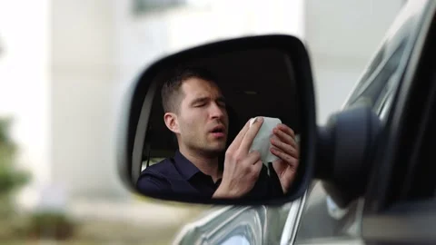 Young man inside car. A view in side mirror of guy sneezing into white tissue Stock Footage 131514040