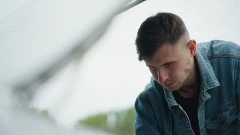 Young man inspecting, Young man assessing car engine under cloudy sky, Male Stock Footage 329432490