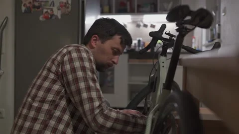 A young man installs a bicycle accessory at home in a studio apartment. A young Video stock 211454612