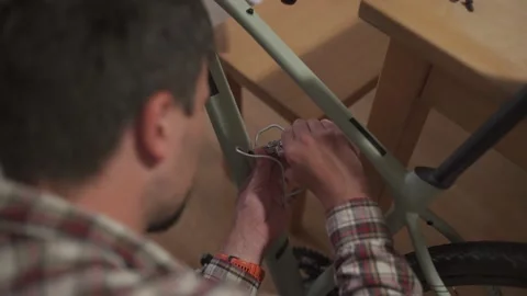A young man installs a bicycle accessory at home in a studio apartment. A young 库存影片 211455232