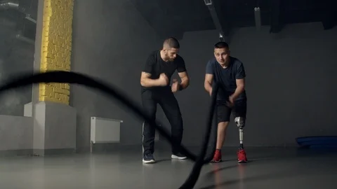 Young man with instructor using battle ropes in gym Stock Footage 125533044