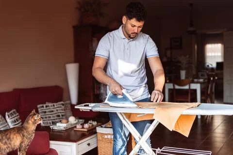 A young man irons while his cat looks at him Stock Photos
