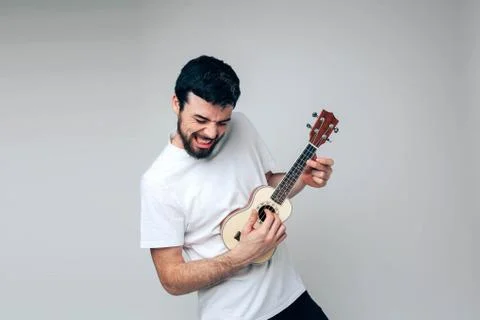 Young man isolated over background. Rocking alone during playing on ukulele 스톡 사진