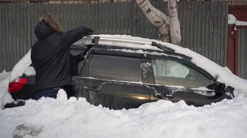 A young man in a jacket cleans his car of snow with a brush. The car was covered Stock Footage 168543875
