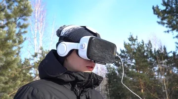 A young man in a jacket, in a hat, in glasses of virtual reality against the bac 库存影片 85994980