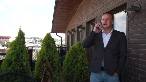 A young man in a jacket is talking on the phone on the terrace. Male Stock Footage 157498286