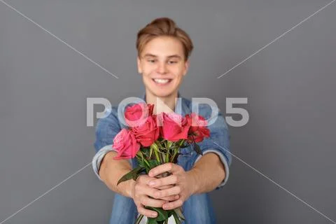 Young man in jeans jacket studio isolated on grey celebration concept with roses Stock Photos
