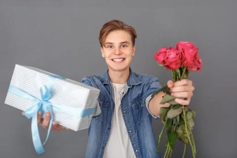 Young man in jeans jacket studio isolated on grey celebration concept with gift Foto stock
