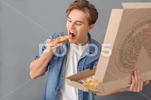 Young man in jeans jacket studio isolated on grey eating pizza slice Stock Photos