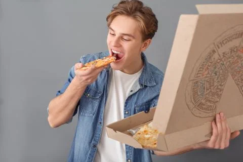 Young man in jeans jacket studio isolated on grey eating pizza slice Stock Photos