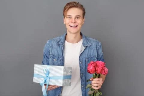 Young man in jeans jacket studio isolated on grey celebration concept with gift Stock Photos