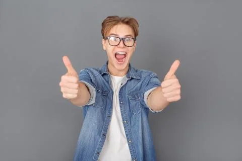 Young man in jeans jacket studio isolated on grey thumbs up joyful Stock Photos
