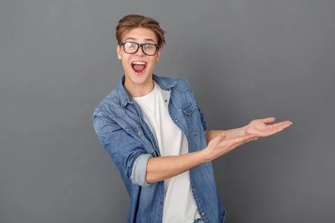 Young man in jeans jacket studio isolated on grey showing copyspace cheerful Stock Photos