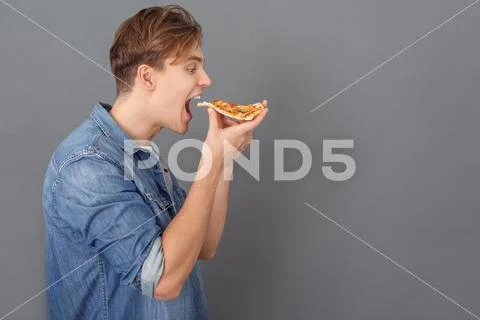 Young man in jeans jacket studio isolated on grey holding pizza sice side view Stock Photos