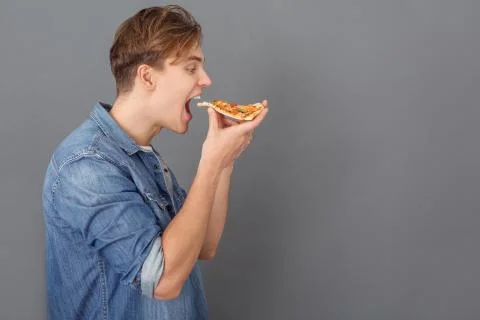 Young man in jeans jacket studio isolated on grey holding pizza sice side view Stock Photos