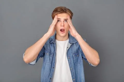 Young man in jeans jacket studio isolated on grey having bad headache Foto stock