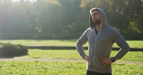 Young man jogger stretching his neck in the beautiful green sunny park. Outdoor Stock Footage 82509930
