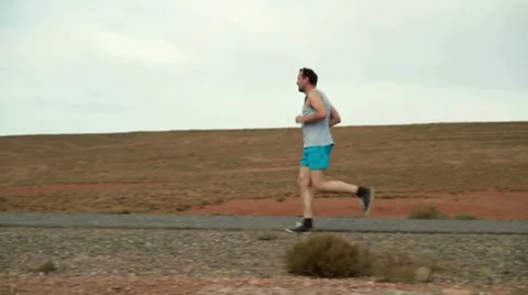 Young man jogging on desert road, slow motion Vídeos de archivo 10842376