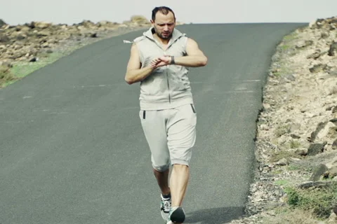 Young man jogging down through road and checking time NTSC Stock Footage 47453278