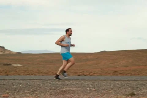 Young man jogging, resting and drinking water on desert road Stockbeeldmateriaal 10834696