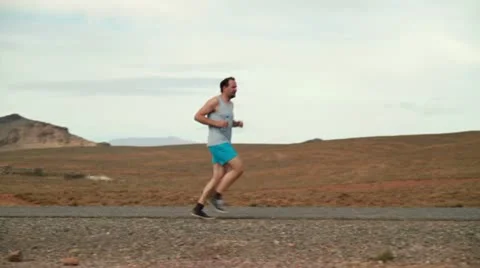 Young man jogging, resting and drinking water on desert road Stockbeeldmateriaal 10834697
