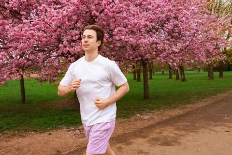 Young man jogging on a trail through a park with blooming pink cherry bloss.. 스톡 사진