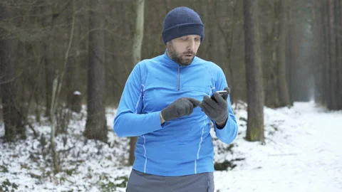 Young man jogging in winter forest and checking time on phone Stock Footage 88676188