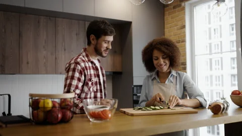 Young man joining his girlfriend who's cooking in the kitchen, couple flirting Stock Footage 231572299